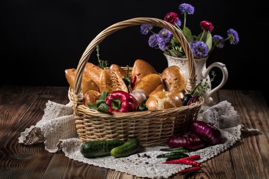 Wicker basket with vegetables and pastries, tablecloth and vase with flowers on an old wooden desk
