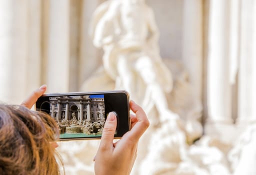Woman taking a photo with a smartphone to the iconic Trevi Fountain in Rome