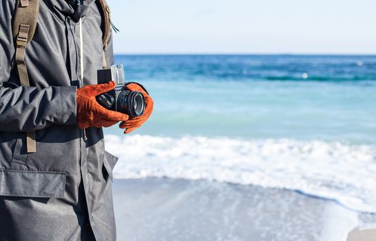 Man hold in hand a vintage old camera on the seashore background