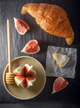 Croissant with soft cheese and figs on a stone plate.