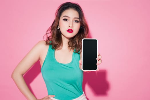 Asian girl with professional makeup showing smartphone screen on pink background.