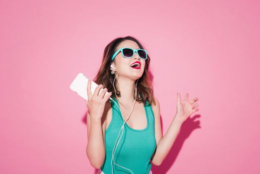 Summer lady. Beautiful asian girl with professional makeup and stylish hairstyle singing and dancing while listening to music on pink background.