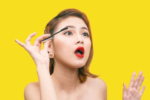 Portrait of Asian Beautiful woman with makeup brush near her face against yellow background