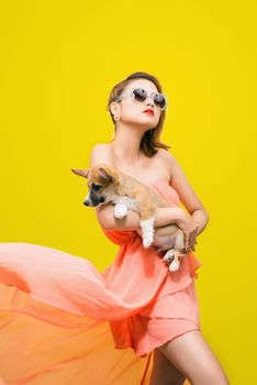 Beautiful young asian woman in nice spring dress, posing in studio with corgi puppy. Fashion photo.