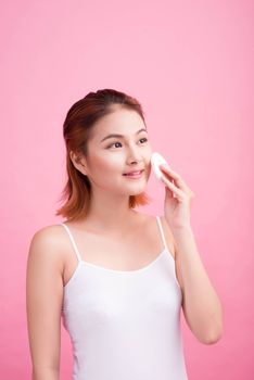 Young lady applying blusher on her face with powder puff, skin care concept on pink background.