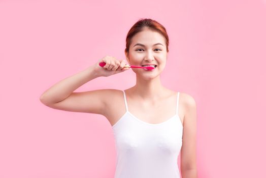 Smiling young woman with healthy teeth holding a tooth brush over pink background.
