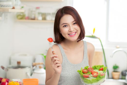 Beautiful young asian girl eating salad. smiling happy girl eating healthy food.