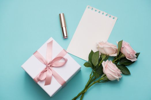 Mother's Day concept. Bouquet of pink roses with gift box and lipstick. Blank paper note for copy space.