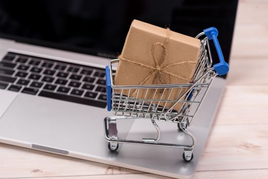 Shopping time. A laptop and shopping cart gift box wrapped with paper kraft on table.