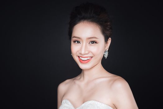 Fashion portrait of beautiful young asian woman in white dress over dark background.