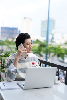 Asian businessman using mobile phone while working with laptop on table in coffee shop