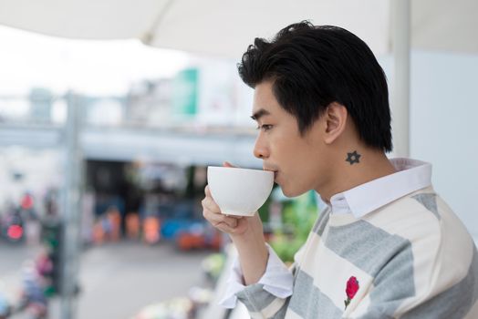 Handsome young man drinking coffee looking out at the view from his home office 