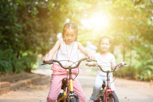 Portrait of active Asian family at nature park. Children biking outdoors. Morning sun flare background.