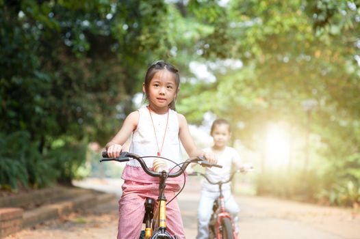 Portrait of active Asian family at nature park. Children riding bicycle outdoors. Morning sun flare background.