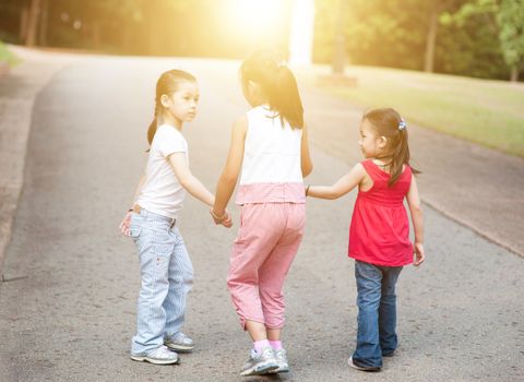 Portrait of Asian children holding hands walking at park. Little girls having fun outdoors. Morning sun flare background.