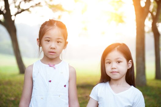 Portrait of Asian children at park. Little girls having fun outdoors. Morning sun flare background.