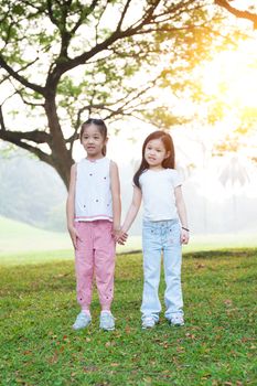 Portrait of Asian kids holding hands at park. Little girls having fun outdoors. Morning sun flare background.