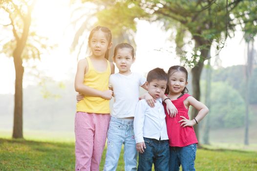 Portrait of four Asian children at park. Little girls and boy having fun outdoors. Morning sun flare background.
