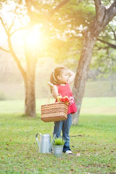 Portrait of curious Asian kid picnic outdoors. Little girl having fun at nature park. Morning sun flare background.