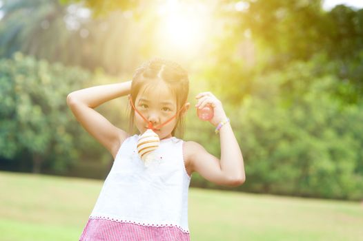 Portrait of Asian child playing toy at park. Little girl having fun outdoors. Morning sun flare background.