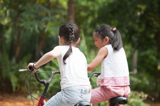 Rear view of active Asian family at nature park. Children cycling outdoors. Morning sun flare background.