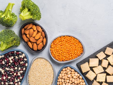 Vegetarian or vegan healthy protein sources concept. Quinoa, chickpea, almond, red lentils, mixed bean, broccoli, tofu on gray concrete background. Close up. Top view or flat lay. Copy space.