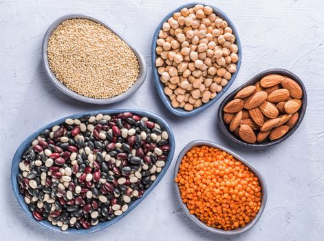 Vegetarian healthy protein sources on gray concrete background. Quinoa, chickpea, almond, red lentils, mixed bean as vegan sources of protein concept. Close up. Top view or flat lay.