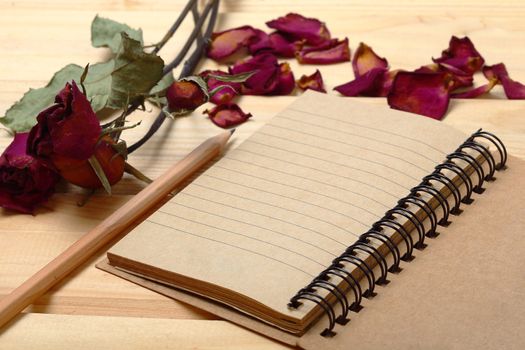 Empty notebook and dry roses with pencil on old wood, eco concept background for valentine.