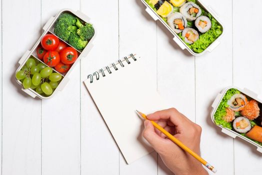 Bento box with different food, fresh veggies and fruits. Notebook with copyspace.