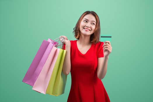 Santa asian woman holding shopping bags and credit card against blue vignette