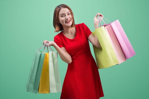 Beautiful young asian woman with colored shopping bags over blue background