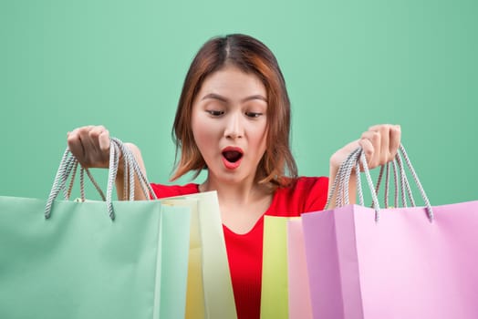 Beautiful young asian woman with colored shopping bags over blue background