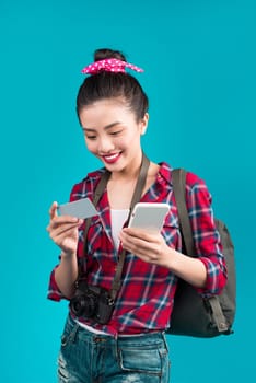 Happy young asian woman holding credit card and smartphone standing over blue.