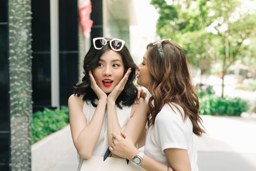 Woman whispering in her friends ears. Two excited friends shopping.