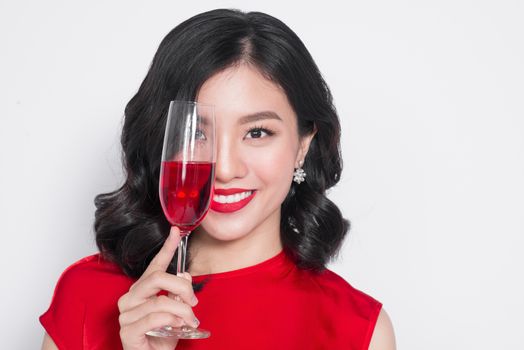 Young celebrating asian woman in red dress holding wine glass.