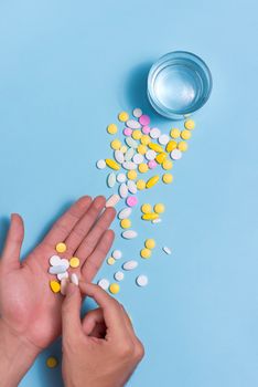 Colored pills in hand with water on blue background.