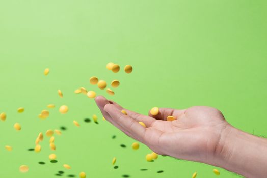 Flying yellow pills from hand in front of green background