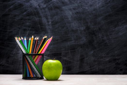 School and office supplies and apple in front of blackboard.