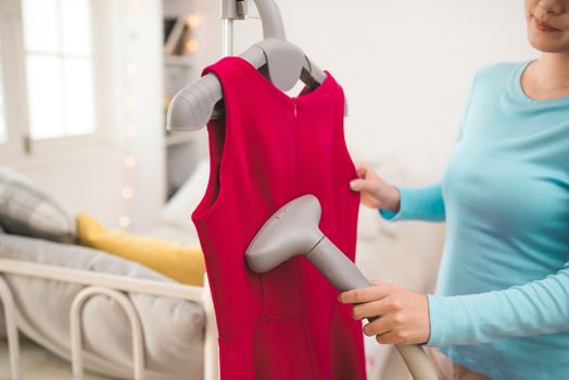 Happy young asian woman steaming clothes in room