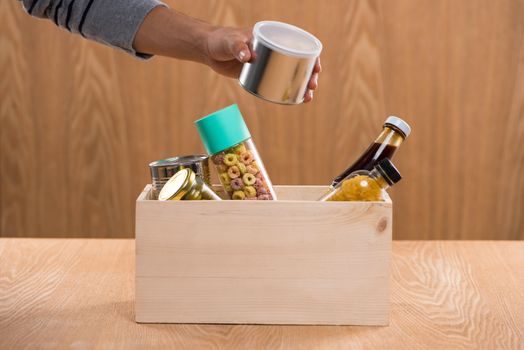 Volunteer with donation box with foodstuffs on wooden background