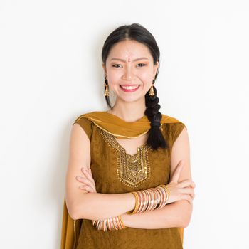 Portrait of arms crossed mixed race Indian Chinese female in traditional Punjabi dress smiling, standing on plain white background.