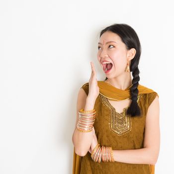 Portrait of shocked mixed race Indian Chinese woman in traditional punjabi dress opened mouth wide, surprised emotion, standing on plain white background.