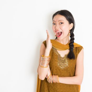 Portrait of shocked mixed race Indian Chinese girl in traditional punjabi dress opened mouth wide, surprised emotion, standing on plain white background.