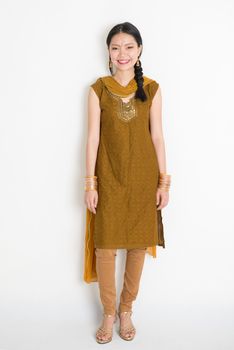 Portrait of young mixed race Indian Chinese girl in traditional punjabi dress smiling, full length standing on plain white background.