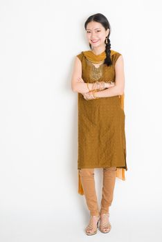 Portrait of young mixed race Indian Chinese female in traditional punjabi dress smiling, full length standing on plain white background.