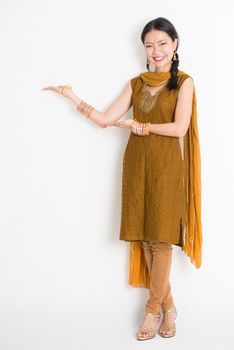 Portrait of young mixed race Indian Chinese woman in traditional punjabi dress hands showing somethings, full length standing on plain white background.