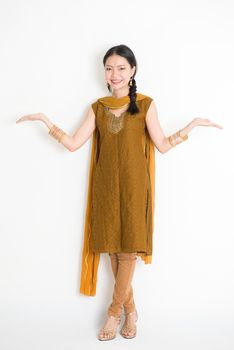 Portrait of young mixed race Indian Chinese woman in traditional punjabi dress hands showing somethings, full length standing on plain white background.