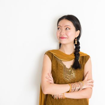 Portrait of arms crossed mixed race Indian Chinese girl in traditional Punjabi dress looking side upward, standing on plain white background.