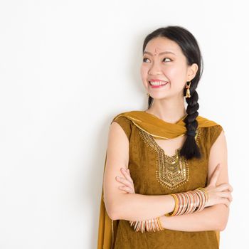 Portrait of arms crossed mixed race Indian Chinese woman in traditional Punjabi dress looking side upward, standing on plain white background.