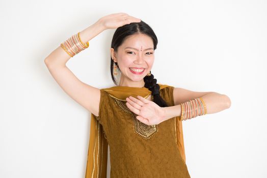 Portrait of young mixed race Indian Chinese female dancer in traditional punjabi dress with dancing pose, standing on plain white background.